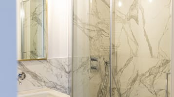 Un bagno moderno con doccia vetro, pareti in marmo e lavandino bianco.