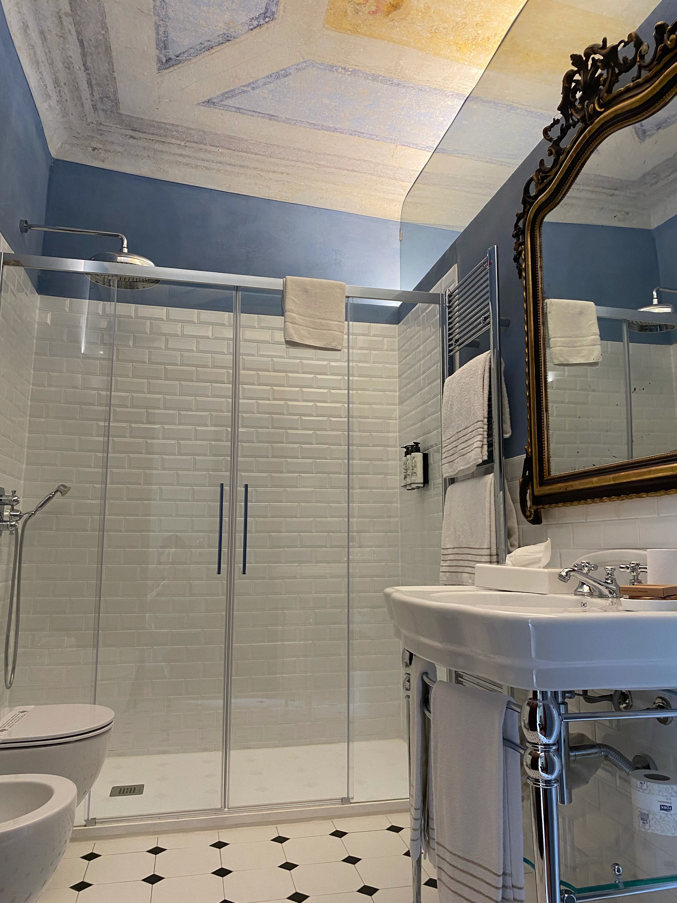 Un bagno moderno con cabina doccia in vetro, piastrelle bianche a metrò quadro, un lavabo bianco con specchio e pavimento a motivi bianchi e neri.