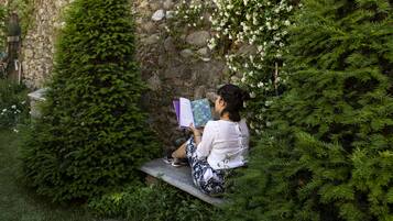 Uma pessoa sentada em um banco num jardim, com um muro de pedra e vegetação.