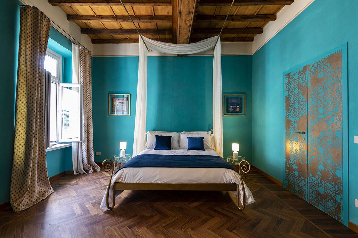 A bedroom with a bed, wooden floor, teal walls, and a wooden ceiling.