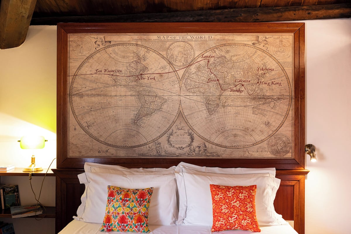 A bed with white linens and two decorative pillows, a wooden headboard, and a large world map above the bed.