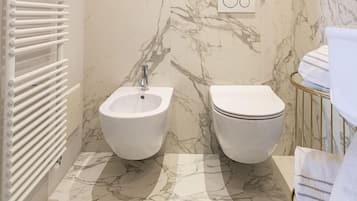 Een badkamer met een bidet, toilet, een marmeren vloer en een lijst met een foto aan de muur.