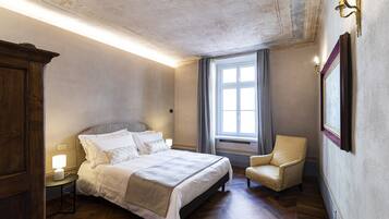 A bedroom with a large bed, a chair, a wardrobe, and a window with curtains.