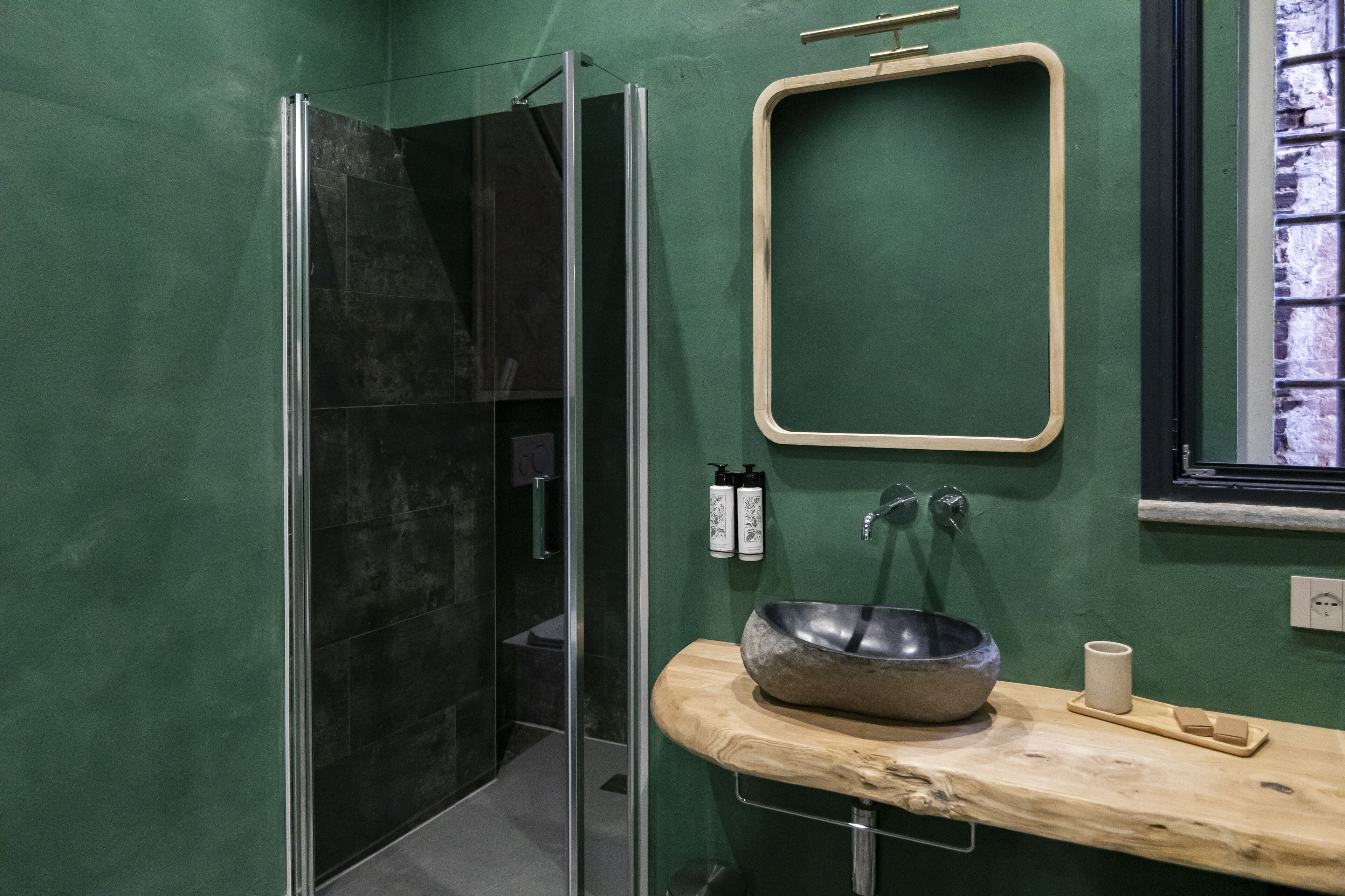 A modern bathroom with a glass shower enclosure, a wooden vanity with a stone sink, and a green wall.