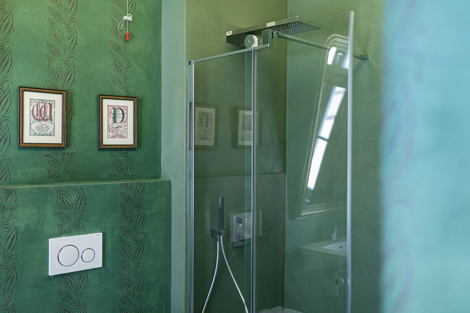 Une salle de bain avec une douche à parois de verre, des œuvres d’art encadrées au mur et un interrupteur visible.