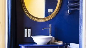Un baño con lavamanos blanco, espejo con marco dorado y tocador azul.