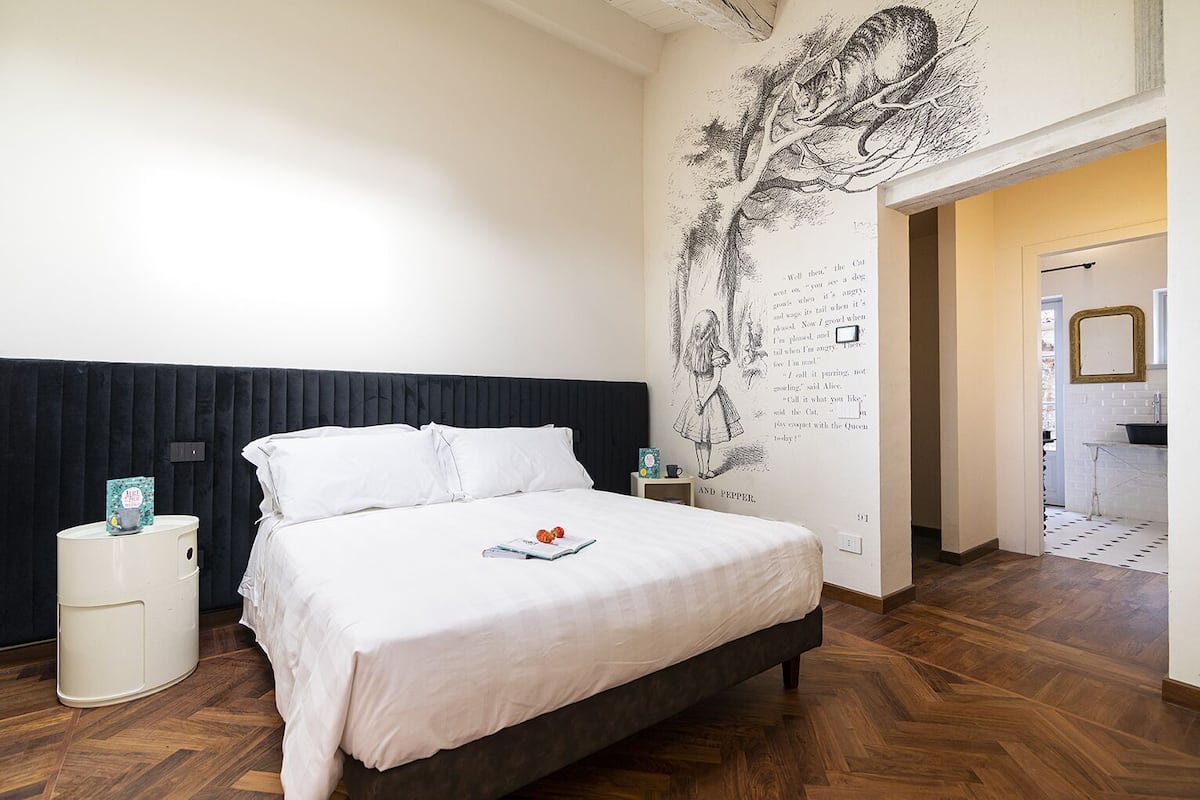 A bedroom with a large bed, a black headboard, a white bedside table, and a wall mural.
