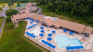 Eine Vogelperspektive eines Resorts mit mehreren Schwimmbecken, Liegebereichen und einem großen Gebäude mit einem markanten Dachdesign.
