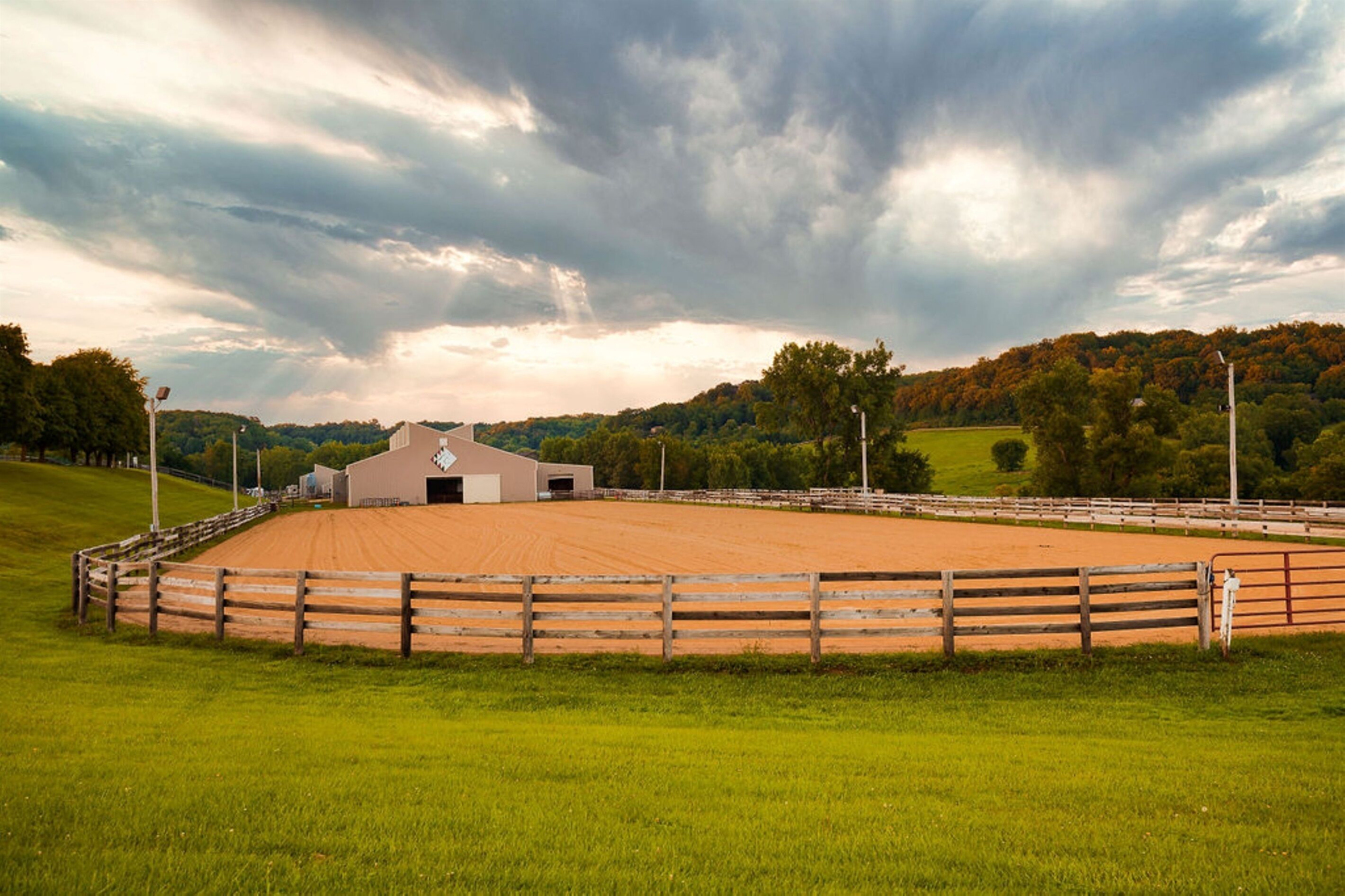 A fenced equestrian arena with a building in the background.