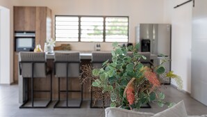 Una cocina moderna con una isla central, taburetes de bar, iluminación colgante y un amplio ventanal que proporciona luz natural.