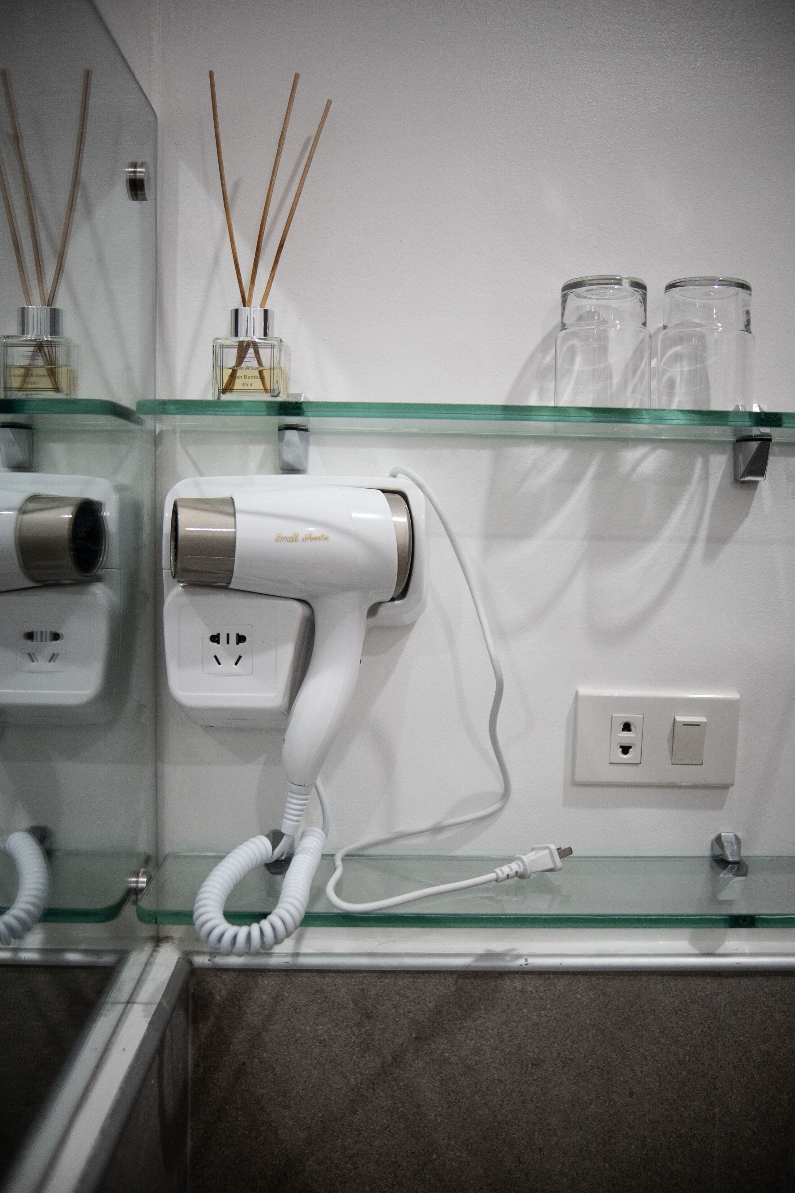 A hairdryer on a glass shelf, a mirror, and a wall socket.