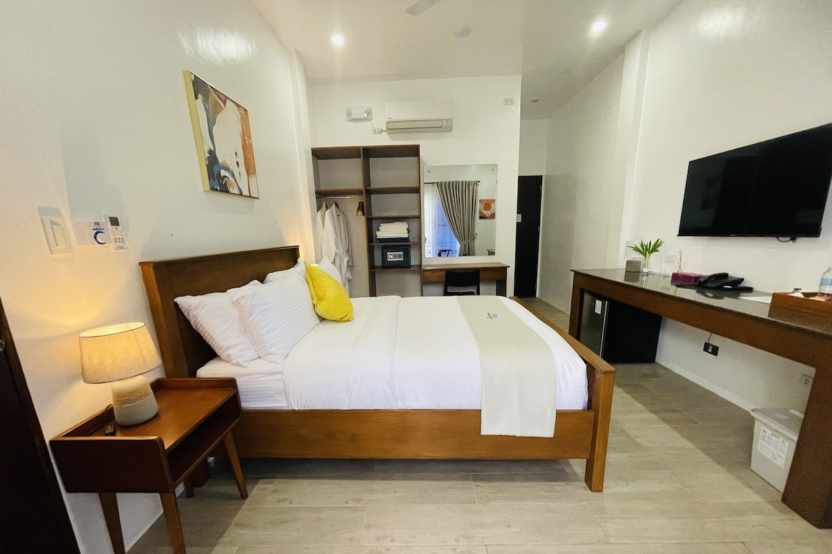Una habitación de hotel con una cama de madera, un escritorio, una silla, un televisor y un armario.