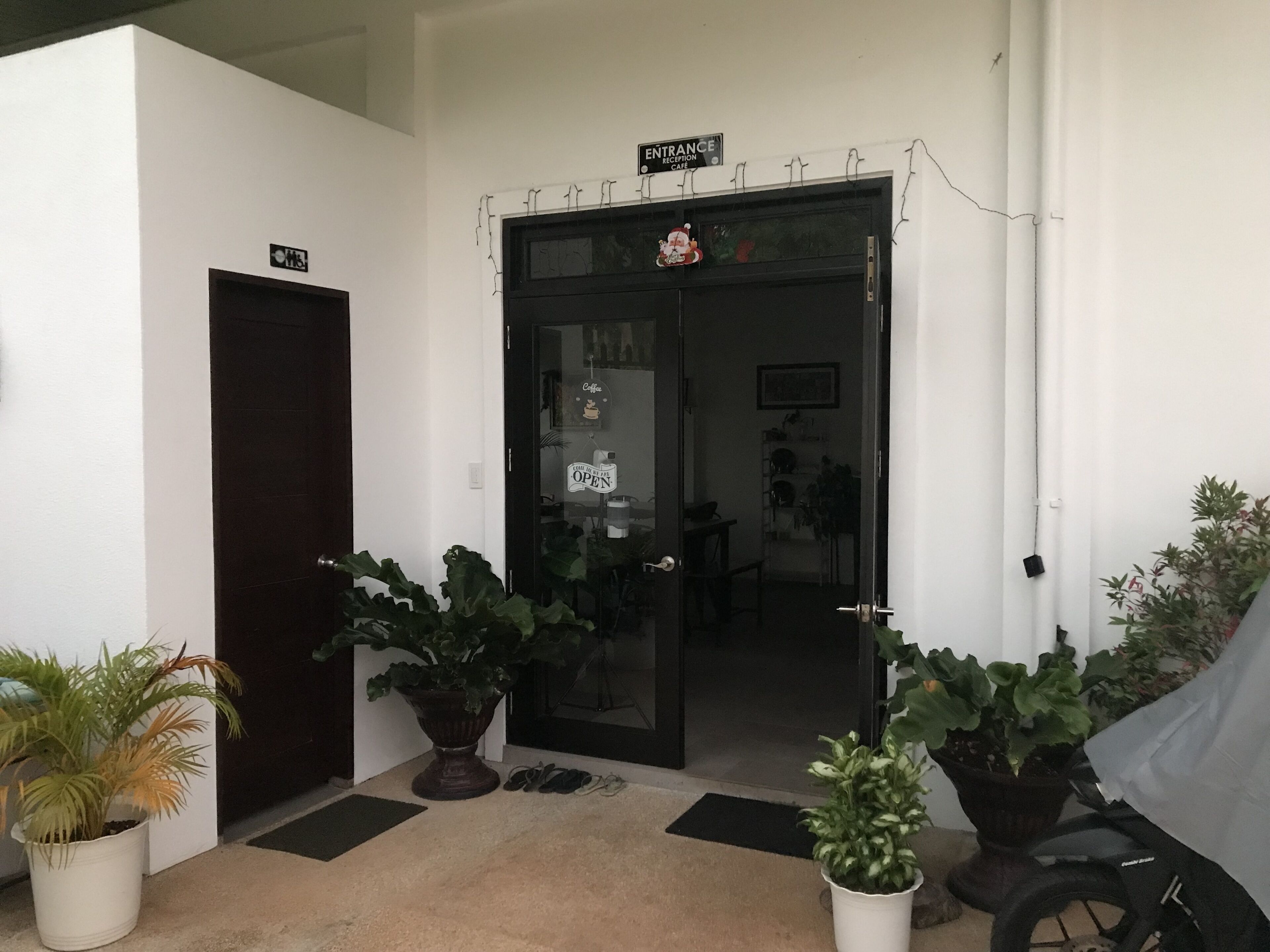 A hotel entrance with a reception desk, a sign indicating the entrance, and several potted plants in front.