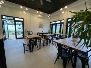 A restaurant interior with multiple tables and chairs, large windows, and hanging pendant lights.