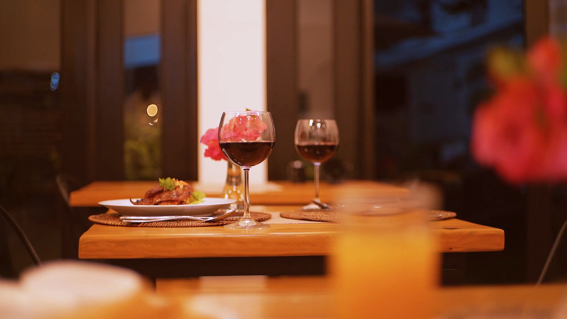 Una mesa de comedor con dos copas de vino y un plato de comida, frente a una ventana con vistas al cielo nocturno.