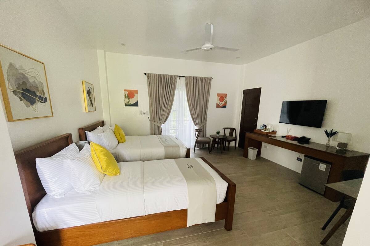 Una habitación de hotel con dos camas, un escritorio, una silla, un televisor y obras de arte en las paredes.