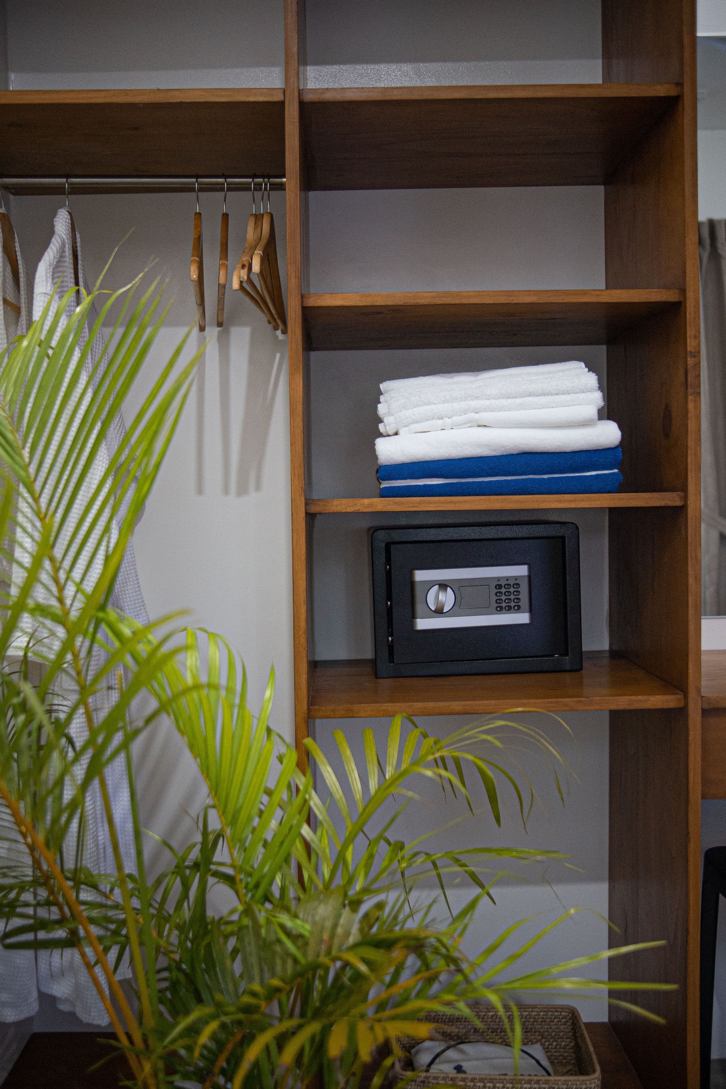 A wooden shelf with folded towels, a safe, and hanging cleaning tools.