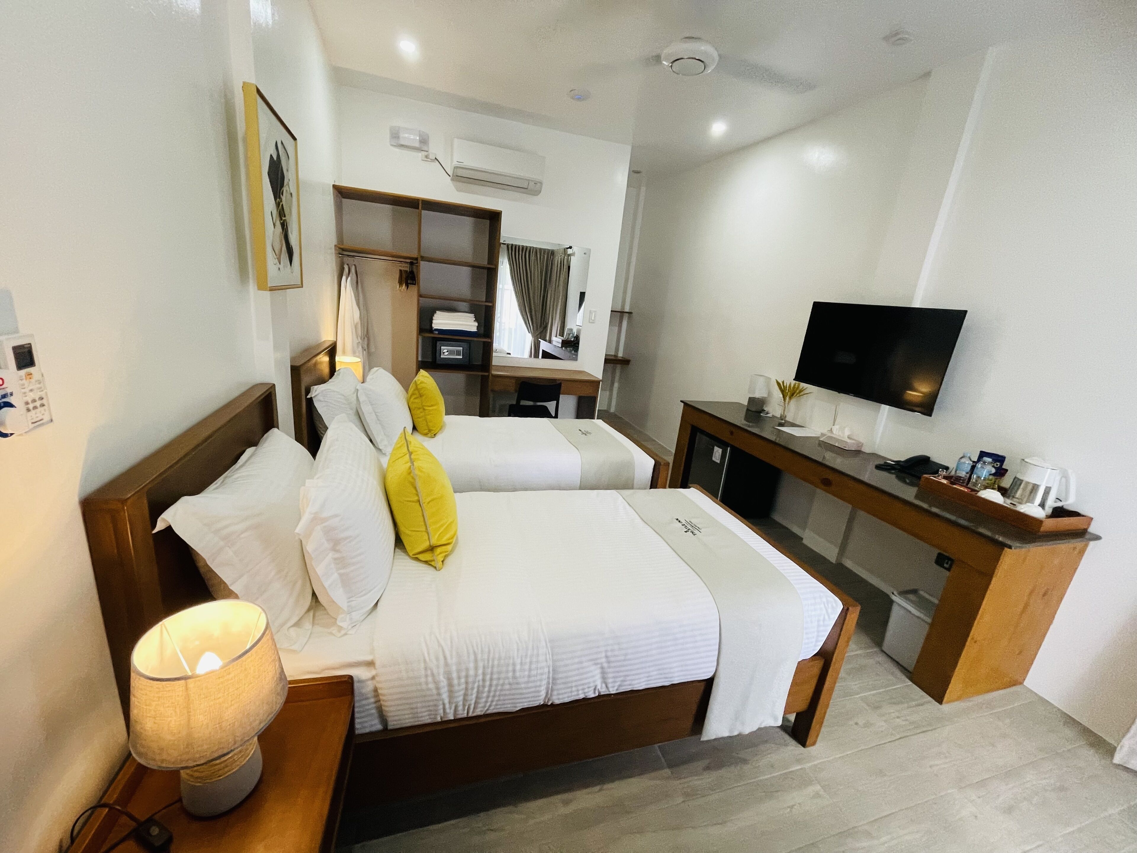 A hotel room with two beds, a desk, a television, and an air conditioning unit.