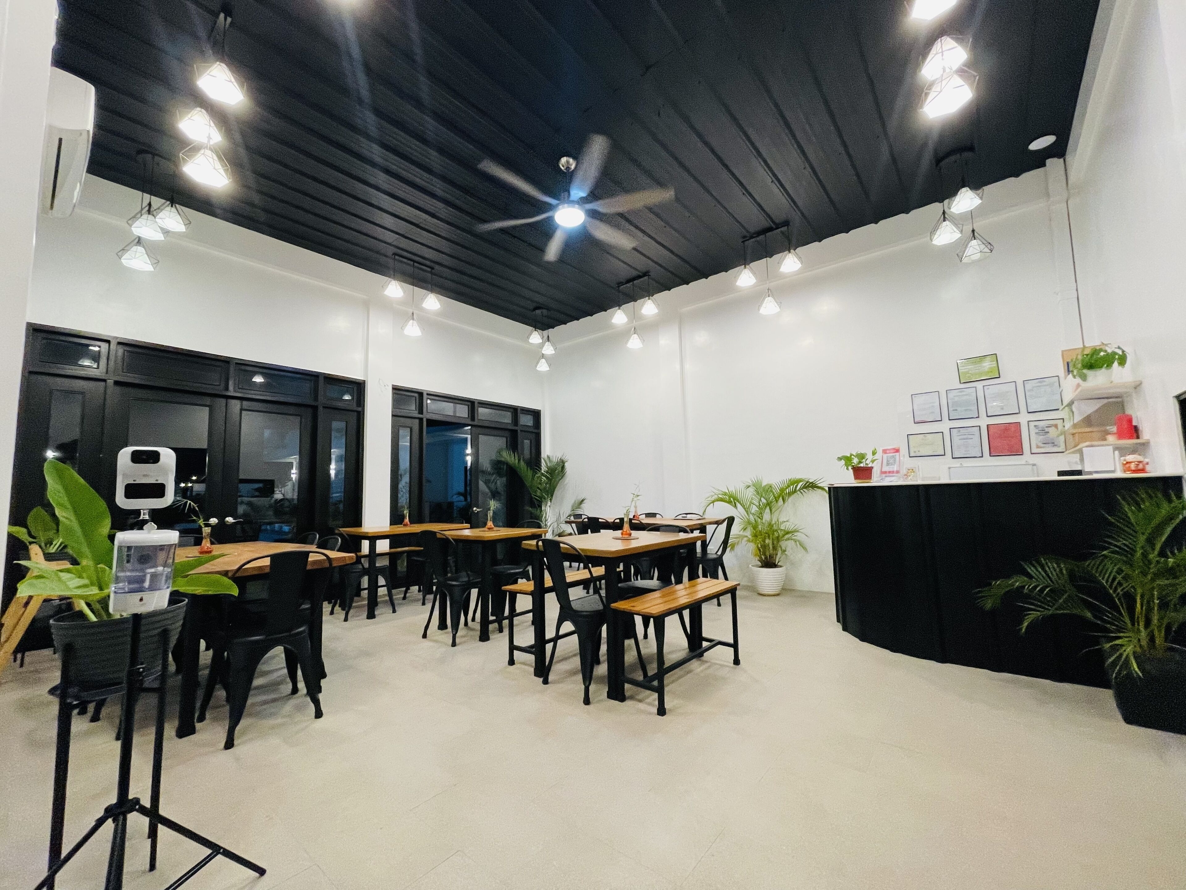 A modern dining area with wooden tables and black chairs, a ceiling fan, and pendant lighting.