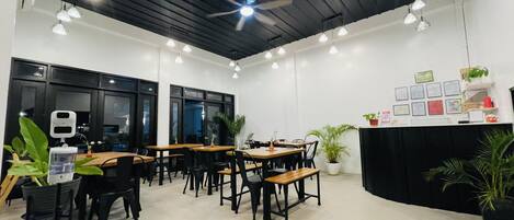 A modern dining area with wooden tables and black chairs, a ceiling fan, and pendant lighting.
