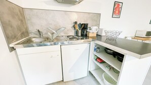 A compact kitchen with a dishwasher, a microwave, and a sink. There is a small shelf with kitchen utensils and a framed picture on the wall. - #EH  |  Le Rousseau 🤍 (Grenoble)