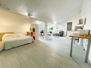 Una habitación amplia con cama, escritorio y sofá. Cuenta con una kitchenette equipada con microondas y lavaplatos.