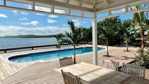 Eine Holzterrasse mit Pool, Sitzgelegenheiten im Freien und Blick auf das Wasser.