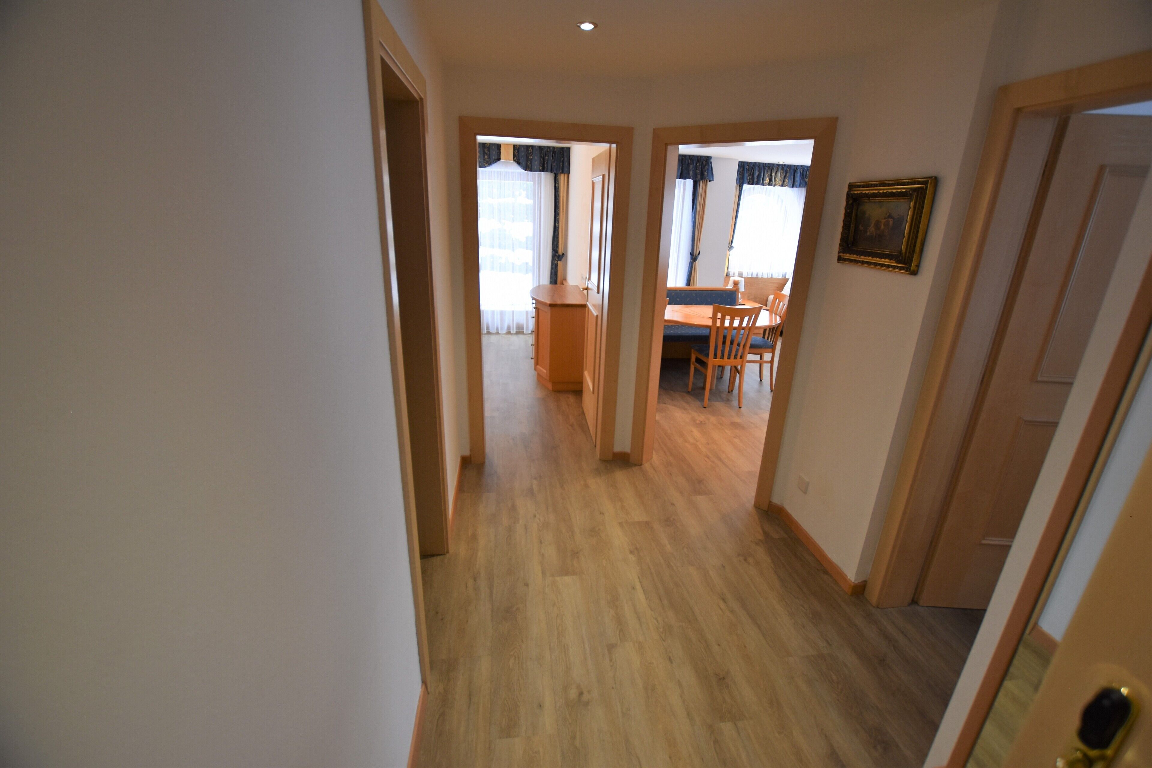 A hallway with wooden flooring leading to a dining area with a table and chairs.