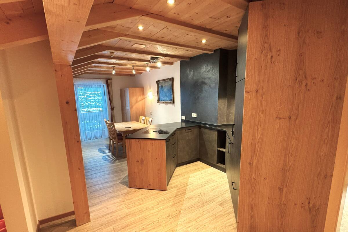 A modern kitchen with wooden beams, a dining area with a table and chairs, and a view of the outdoors.