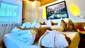 A hotel room with a wooden ceiling, a bed with towels, a window with curtains, and a wall-mounted picture. - Residence Palmai (Castelrotto)