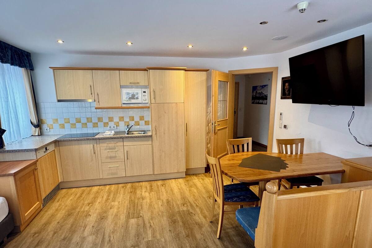 A compact kitchen with wooden cabinets, a built-in microwave, and a dining area with a table and chairs.