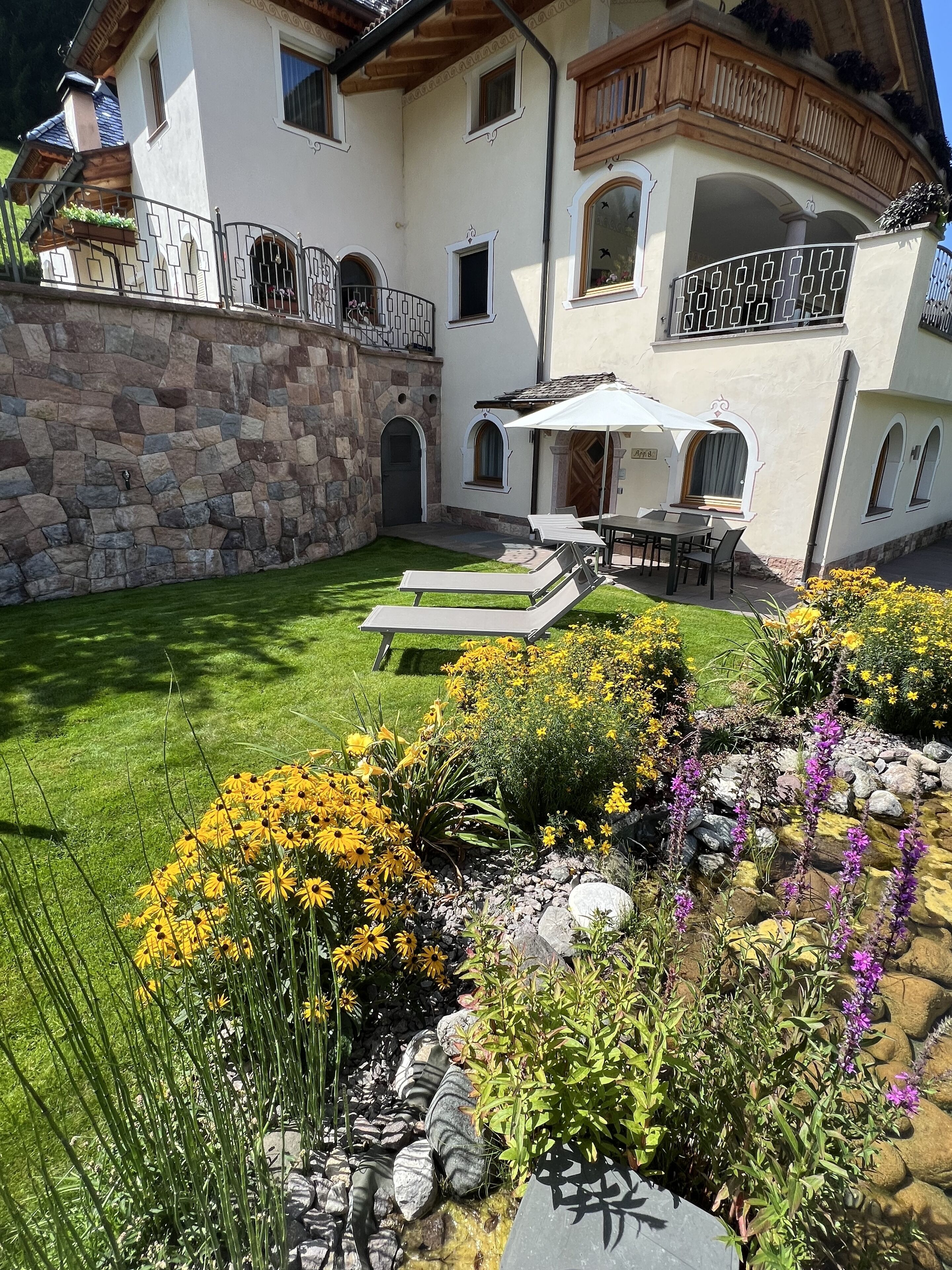 A two-story house with a stone wall, a balcony, and a small patio with a table and chairs.