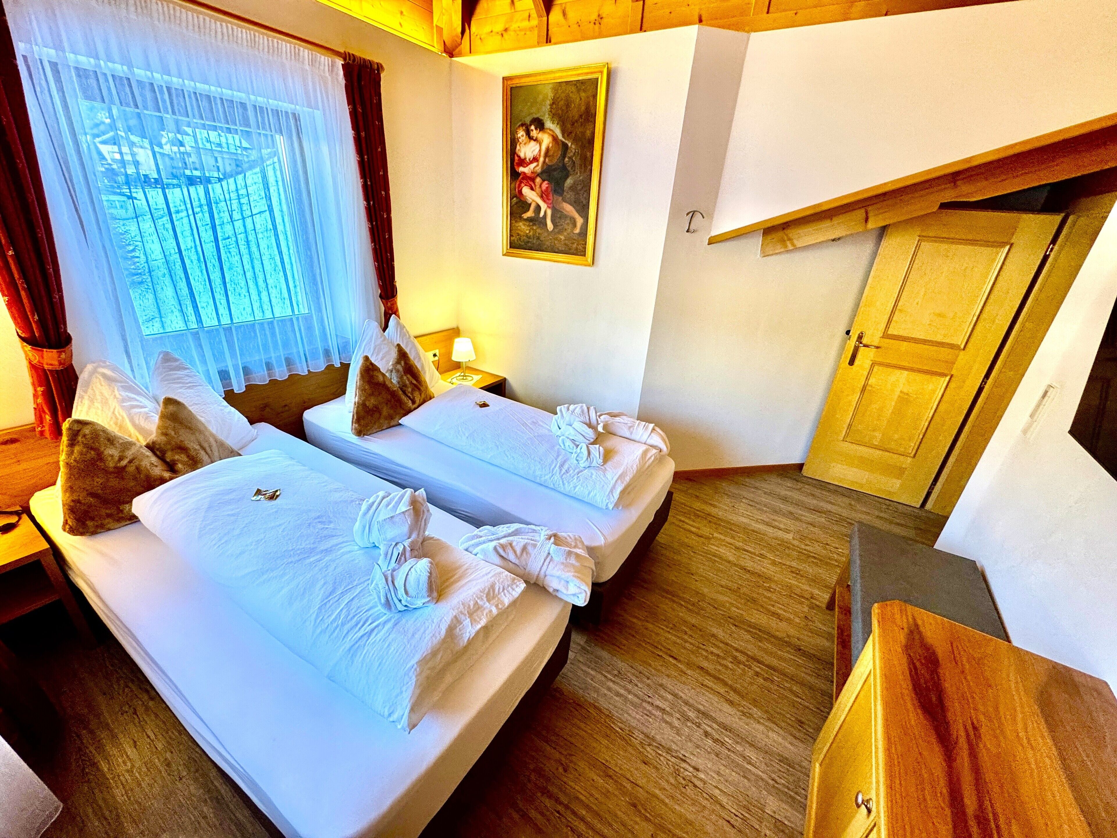 A hotel room with two beds, a painting on the wall, and a wooden ceiling.