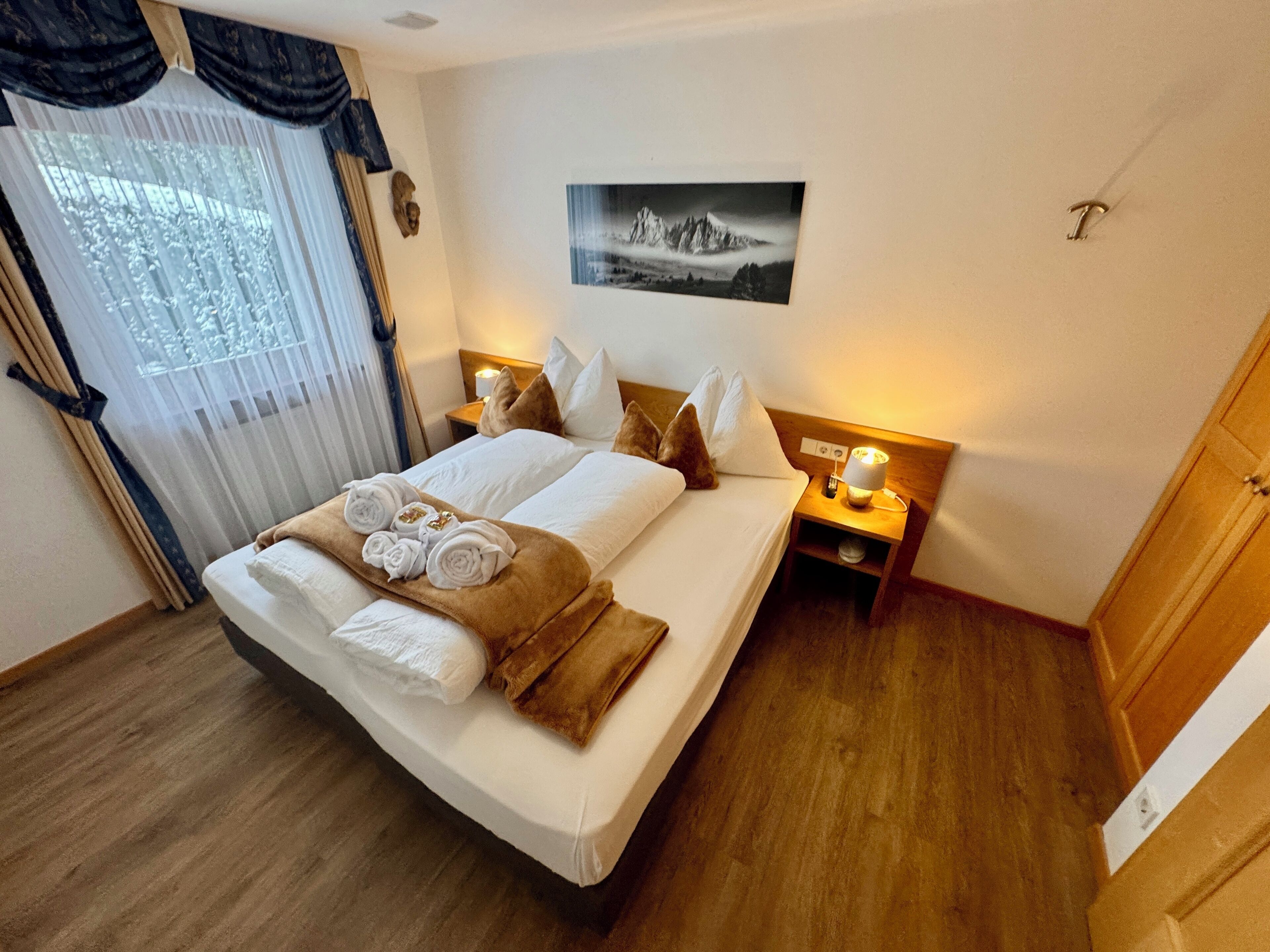 Ein ordentlich bezogenes Bett mit Handtüchern, ein Nachttisch mit Lampe und ein gerahmtes Bild an der Wand.