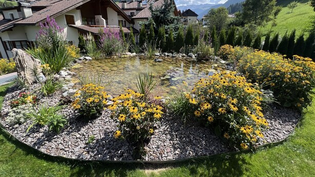 A garden with a pond, surrounded by colorful flowers and a mountainous backdrop. - Residence Palmai (Castelrotto)