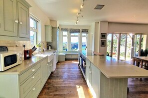 A kitchen with a central island, wooden flooring, and large windows. - White Horses Bantham South Devon (Bantham)