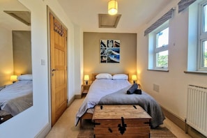 Une chambre à coucher avec un lit, des lampes de chevet, une commode en bois, un tableau accroché au mur et une fenêtre.