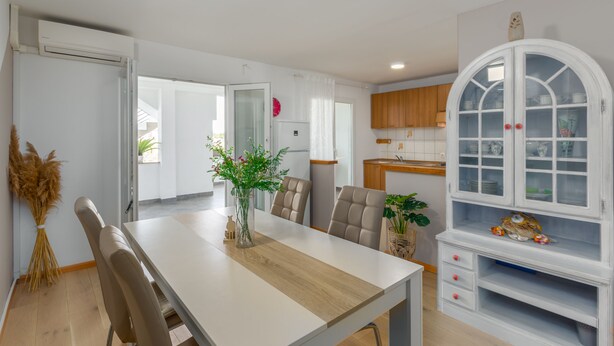 Eine moderne Küche mit weißen Schränken, einem Holzespeise Tisch und einem großen, weißen Schrank mit Glastüren.