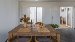 Ein Essbereich mit Holztisch, Korbstühlen, einer Blumenvase, Obstschale und einer Weinflasche.