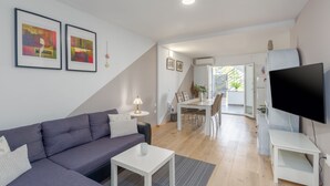 Ein modernes Wohnzimmer mit einer Couch, einem Couchtisch, einem Fernseher und einem Essbereich mit Stühlen und einem Tisch.