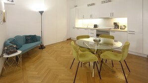 Une cuisine moderne avec des meubles blancs, une machine à café et une table à manger en verre, entourée de chaises vertes.