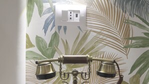 Un vieux téléphone à cadran, posé sur une petite table ronde, devant un mur orné d’un motif de feuilles tropicales.