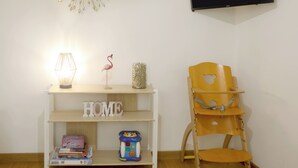 Une pièce avec une console blanche où sont exposés des livres et une lampe, une décoration en forme de flamant rose, une chaise en bois et un téléviseur fixé au mur qui affiche le logo « NETFLIX ».