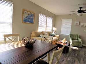 A dining area with a wooden table, white chairs, a beige sofa, and a green armchair. - The Aviator's Landing (Pensacola)