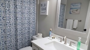 A bathroom with a floral patterned shower curtain, a toilet, a sink with a mirror, and a towel rack.