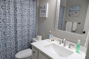 A bathroom with a floral patterned shower curtain, a toilet, a sink with a mirror, and a towel rack.