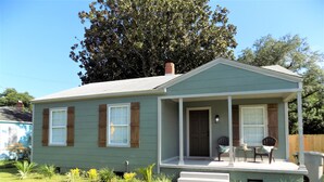 A single-story house with a front porch, a chimney, and a small garden area.