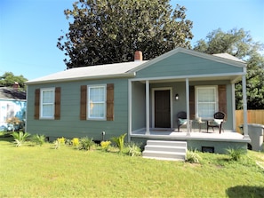 A single-story house with a front porch, a chimney, and a small garden area.