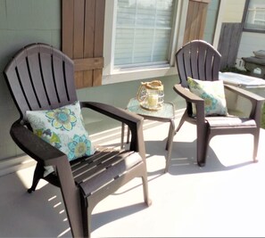 Two Adirondack chairs with floral cushions on a porch with a small table and a lantern. - The Aviator's Landing (Pensacola)