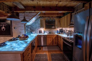 A kitchen with wooden cabinets, a stainless steel refrigerator, and a stone wall.